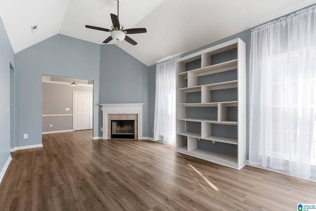 unfurnished living room with lofted ceiling, hardwood / wood-style floors, a wealth of natural light, a tiled fireplace, and built in shelves