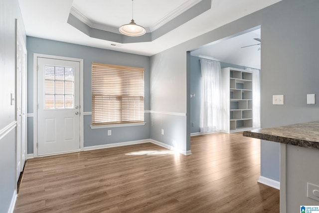 unfurnished dining area featuring ceiling fan, ornamental molding, wood-type flooring, and a tray ceiling