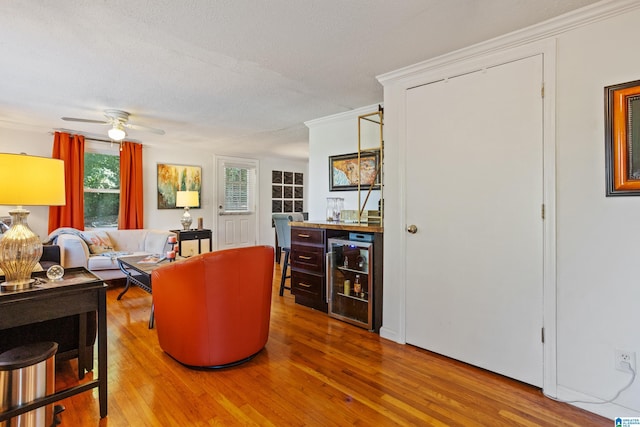 living room with hardwood / wood-style floors, ceiling fan, ornamental molding, a textured ceiling, and indoor bar