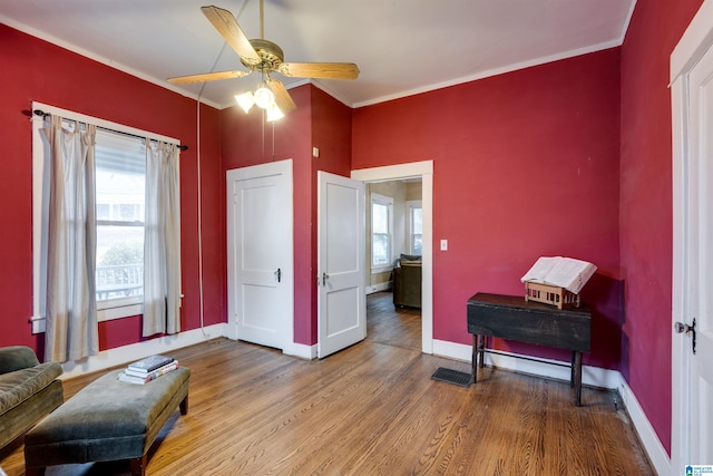 living area featuring hardwood / wood-style flooring, ceiling fan, and crown molding