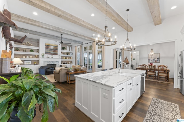 kitchen with light stone counters, white cabinetry, a center island with sink, pendant lighting, and a high end fireplace