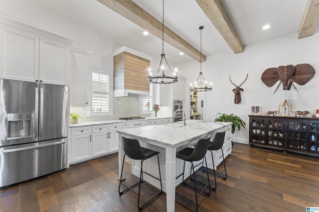 kitchen featuring a kitchen island with sink, stainless steel appliances, light stone counters, white cabinets, and decorative light fixtures