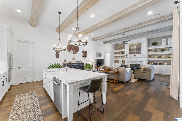 kitchen featuring pendant lighting, light stone counters, an island with sink, and white cabinets