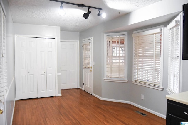 unfurnished bedroom featuring rail lighting, hardwood / wood-style floors, and a textured ceiling