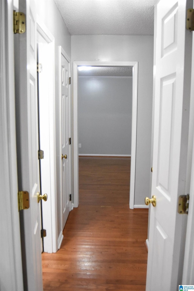 corridor with a textured ceiling and hardwood / wood-style flooring