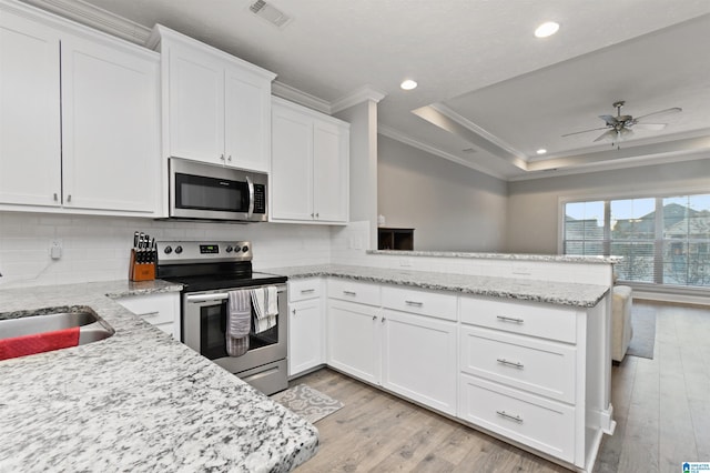 kitchen with appliances with stainless steel finishes, white cabinets, kitchen peninsula, and a tray ceiling