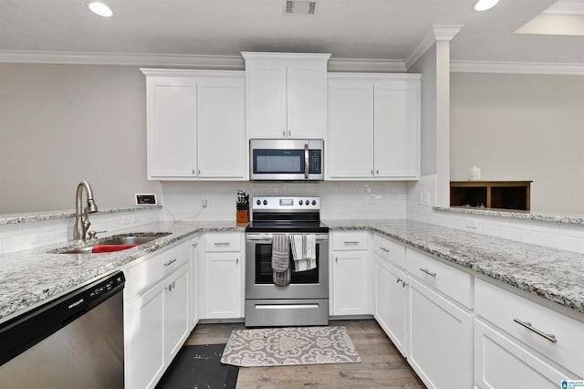 kitchen with appliances with stainless steel finishes, white cabinetry, light stone counters, and sink