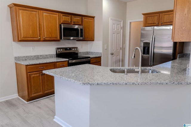 kitchen with light stone counters, appliances with stainless steel finishes, kitchen peninsula, and sink