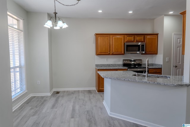 kitchen featuring appliances with stainless steel finishes, sink, a chandelier, light stone counters, and light hardwood / wood-style floors