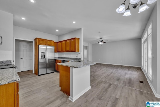 kitchen with sink, stainless steel fridge, light stone countertops, decorative light fixtures, and kitchen peninsula