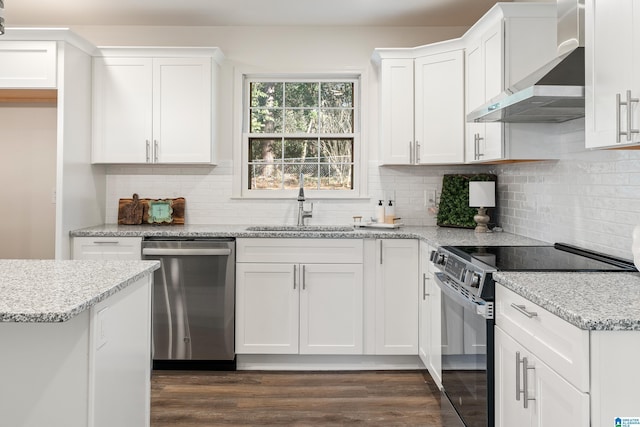 kitchen featuring light stone countertops, appliances with stainless steel finishes, wall chimney exhaust hood, white cabinetry, and sink