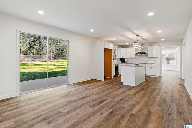 kitchen featuring white cabinetry, light hardwood / wood-style floors, decorative light fixtures, a kitchen island, and wall chimney exhaust hood