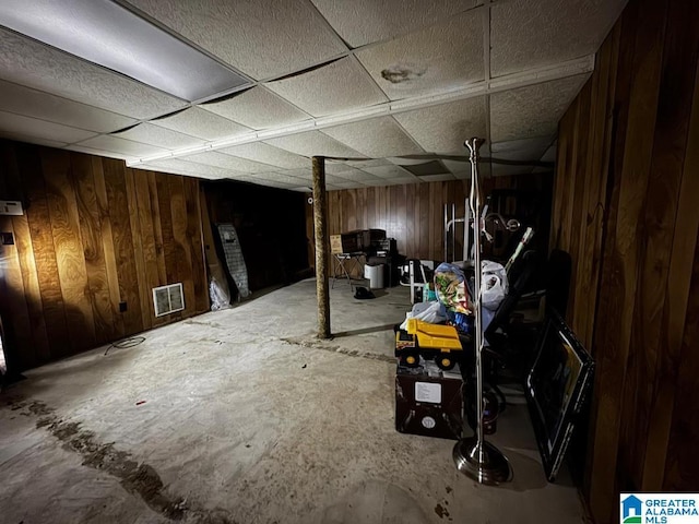 basement with a paneled ceiling and wooden walls