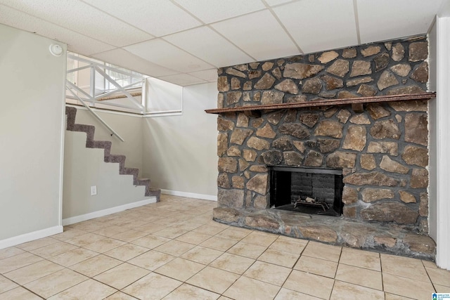 basement with light tile patterned floors, a paneled ceiling, and a stone fireplace