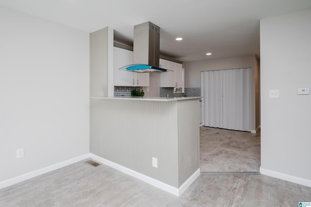 kitchen with white cabinets, backsplash, island exhaust hood, and kitchen peninsula