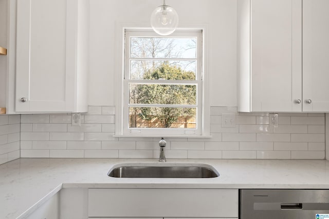 kitchen featuring pendant lighting, dishwasher, white cabinetry, sink, and light stone counters