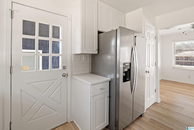 kitchen with stainless steel refrigerator with ice dispenser, backsplash, white cabinets, and light wood-type flooring