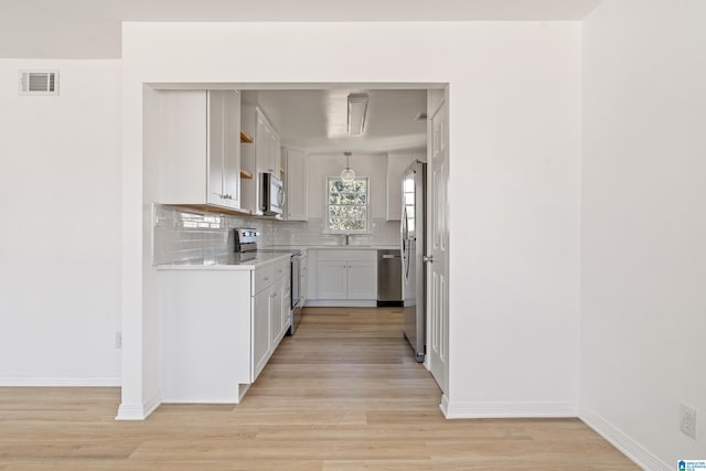 kitchen featuring tasteful backsplash, decorative light fixtures, white cabinetry, light hardwood / wood-style flooring, and appliances with stainless steel finishes