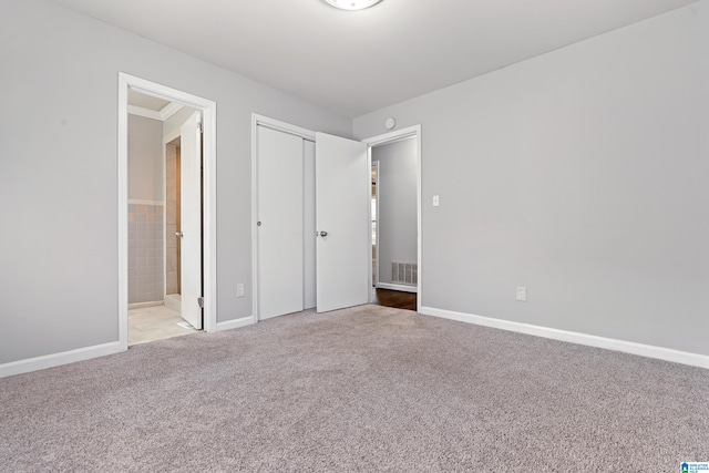 unfurnished bedroom featuring ensuite bathroom, light colored carpet, and a closet