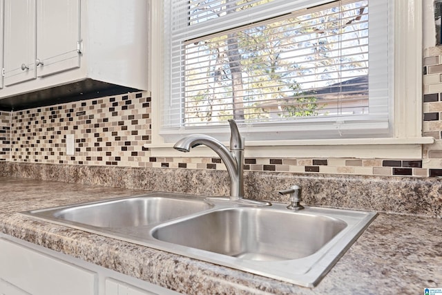 interior details with decorative backsplash, sink, and white cabinets