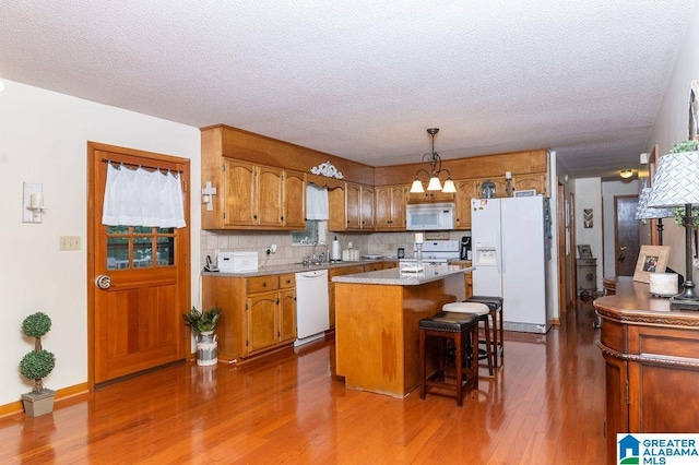 kitchen with a kitchen island, decorative backsplash, sink, white appliances, and hanging light fixtures