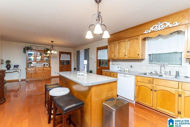 kitchen with light hardwood / wood-style floors, a kitchen island, sink, white dishwasher, and hanging light fixtures