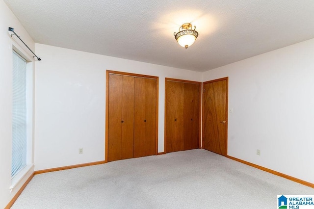 unfurnished bedroom featuring light carpet, a textured ceiling, and two closets