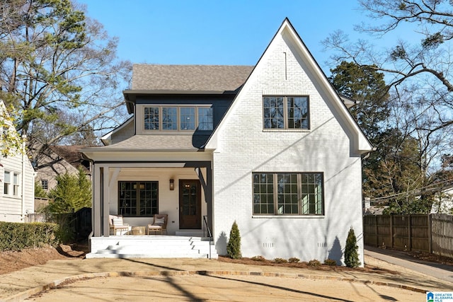 tudor home with roof with shingles, crawl space, covered porch, fence, and brick siding