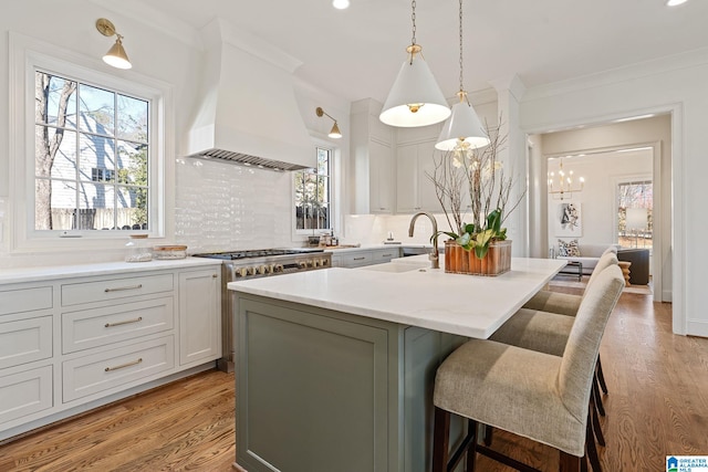 kitchen featuring pendant lighting, a kitchen island with sink, tasteful backsplash, custom range hood, and a kitchen bar