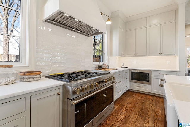 kitchen with stainless steel stove, premium range hood, white cabinets, built in microwave, and decorative backsplash