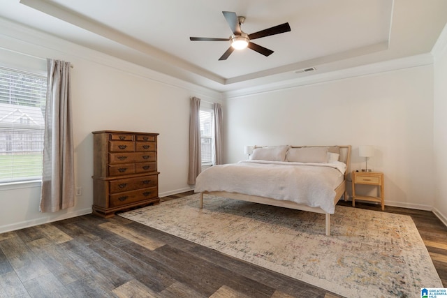 bedroom with dark wood-type flooring, ceiling fan, ornamental molding, and a tray ceiling