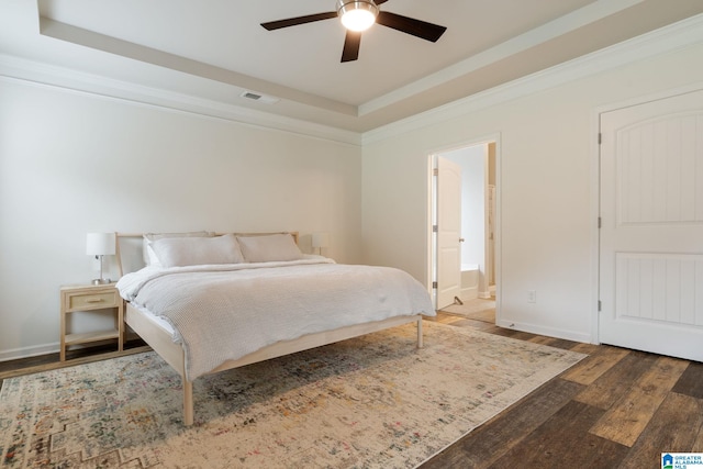 bedroom featuring ceiling fan, connected bathroom, a tray ceiling, and dark hardwood / wood-style floors