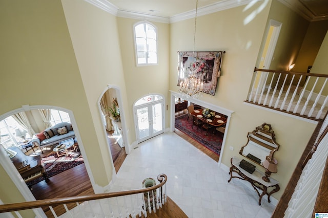 foyer featuring a towering ceiling, french doors, a chandelier, light hardwood / wood-style flooring, and crown molding