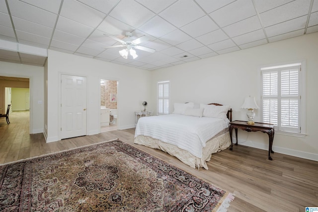 bedroom with hardwood / wood-style floors, a drop ceiling, connected bathroom, and ceiling fan