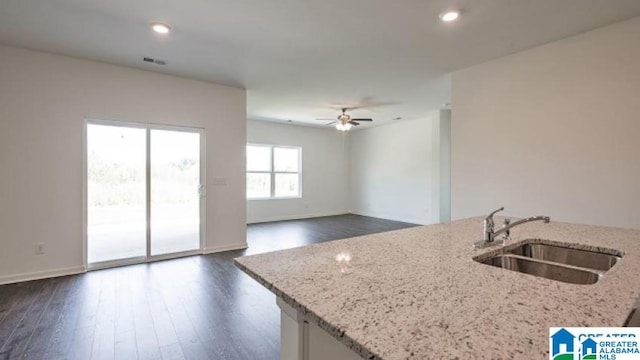 kitchen featuring a kitchen island with sink, sink, dark hardwood / wood-style flooring, ceiling fan, and light stone counters