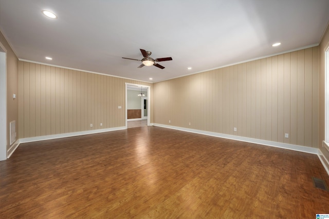 empty room with dark wood-type flooring, ceiling fan, ornamental molding, and wood walls