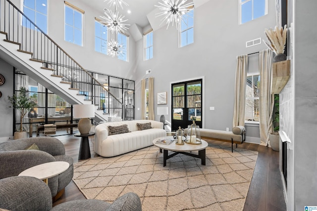 living room featuring wood-type flooring, a healthy amount of sunlight, a towering ceiling, and an inviting chandelier