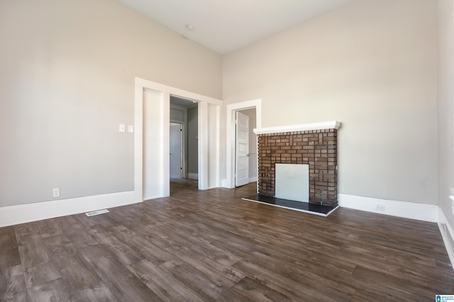 unfurnished living room featuring dark wood-type flooring, a towering ceiling, and a brick fireplace