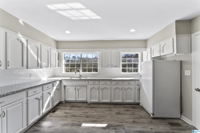 kitchen with dark wood-type flooring, light stone countertops, white refrigerator, white cabinets, and sink