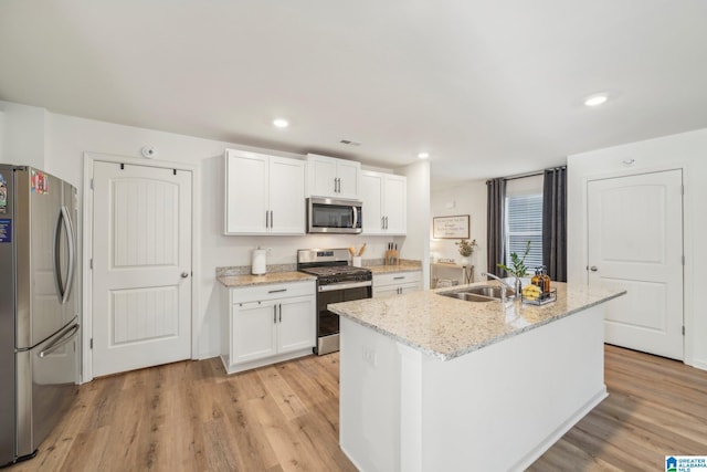 kitchen with light stone countertops, white cabinets, appliances with stainless steel finishes, an island with sink, and sink