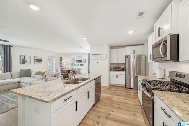 kitchen featuring white cabinets, appliances with stainless steel finishes, sink, a kitchen island with sink, and light stone counters