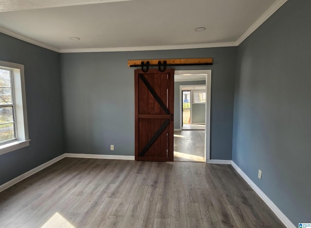 empty room featuring wood-type flooring, ornamental molding, and a barn door