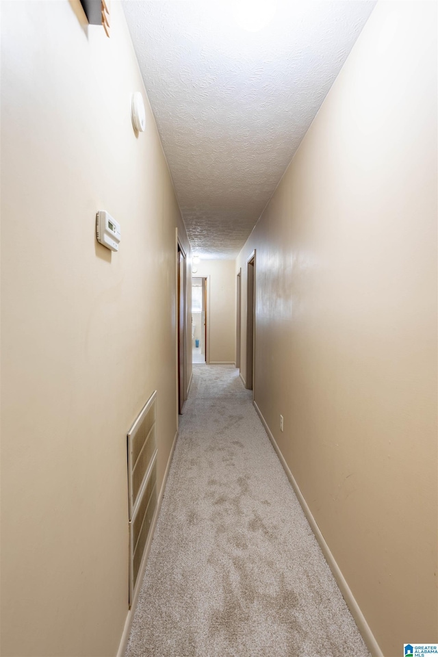 hall with a textured ceiling and light colored carpet