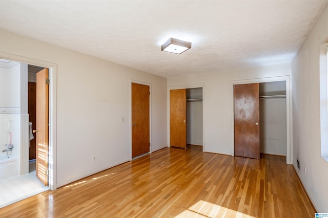 unfurnished bedroom featuring multiple closets, ensuite bathroom, and light hardwood / wood-style floors