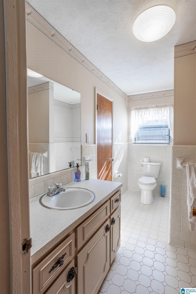 bathroom with toilet, a textured ceiling, tile walls, and vanity