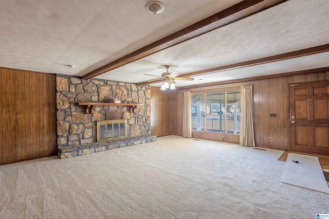 unfurnished living room with wooden walls, a fireplace, a textured ceiling, carpet flooring, and beamed ceiling