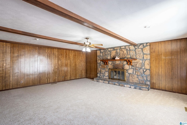 unfurnished living room featuring ceiling fan, a fireplace, beamed ceiling, wooden walls, and light carpet