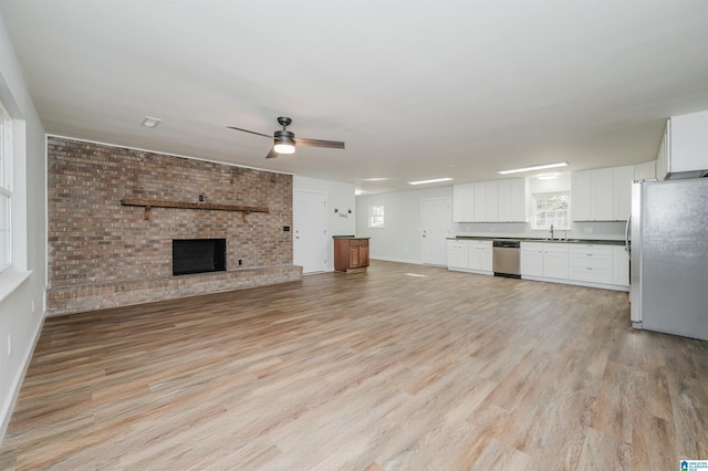 unfurnished living room with a fireplace, brick wall, sink, light hardwood / wood-style flooring, and ceiling fan