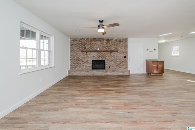 unfurnished living room featuring ceiling fan, a brick fireplace, a healthy amount of sunlight, and light hardwood / wood-style floors