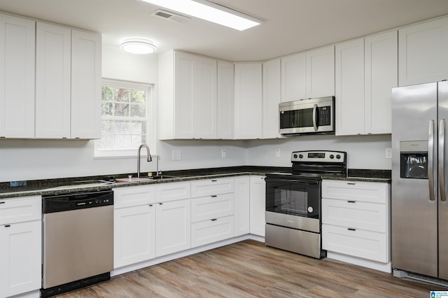 kitchen featuring white cabinets, stainless steel appliances, dark stone countertops, sink, and light wood-type flooring